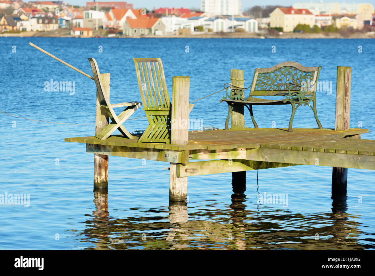 Eine Reihe von alten Gartenmöbel stehen am Ende eines hölzernen Pier mit Stadtbild im Hintergrund unscharf. Stockfoto