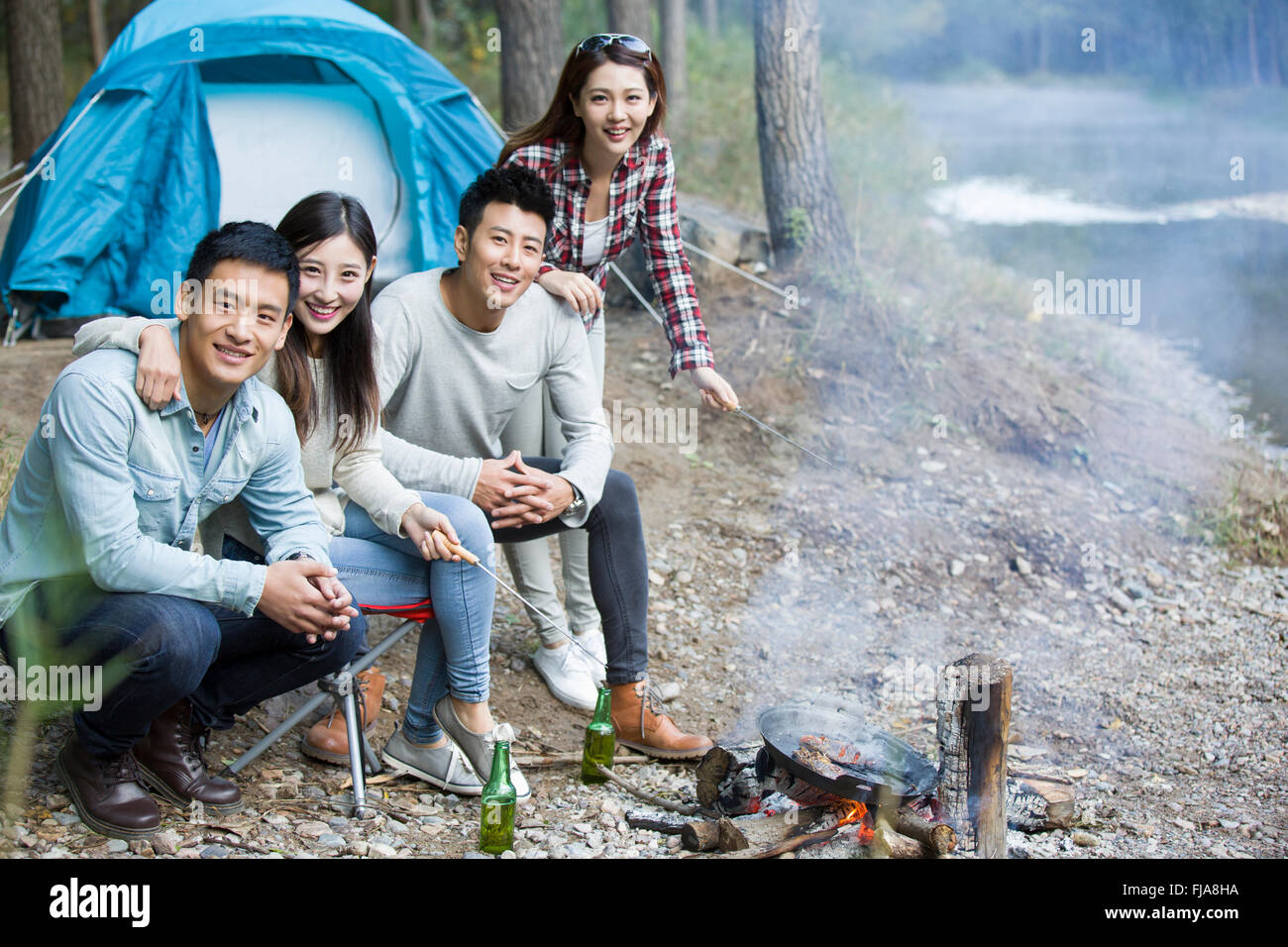 Junge chinesische Freunde sitzen neben Lagerfeuer zubereiten Stockfoto