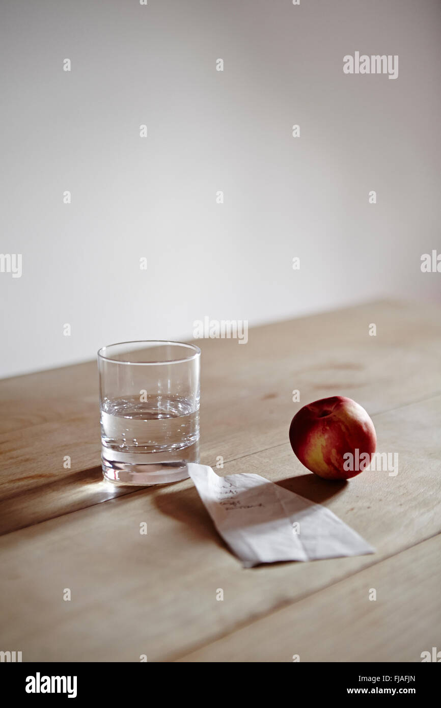 Ein Glas Wasser, eine Nektarine und einen Einkaufszettel auf dem Küchentisch. Stockfoto