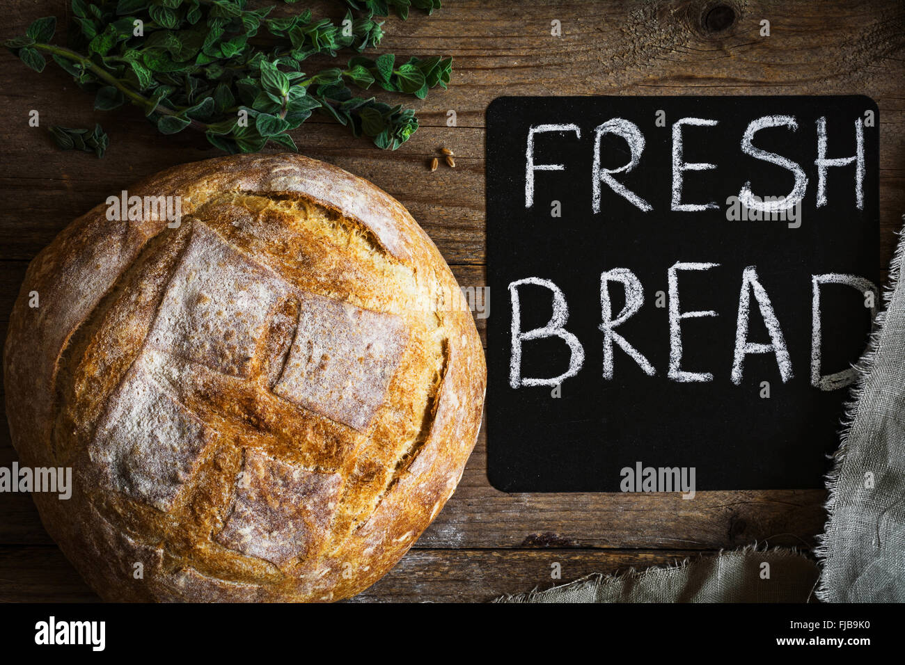 Runden Laib Brot gebackene frisch Sauerteigbrot auf hölzernen Hintergrund. Tafel und Bündel von Weizen Ohr Federn auf Seite Stockfoto