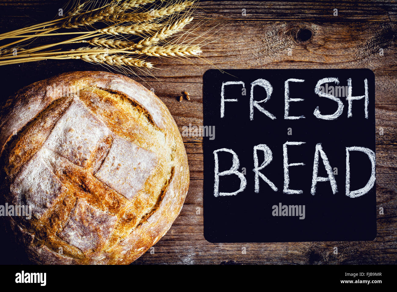 Runden Laib Brot gebackene frisch Sauerteigbrot auf hölzernen Hintergrund. Tafel und Bündel von Weizen Ohr Federn auf Seite Stockfoto