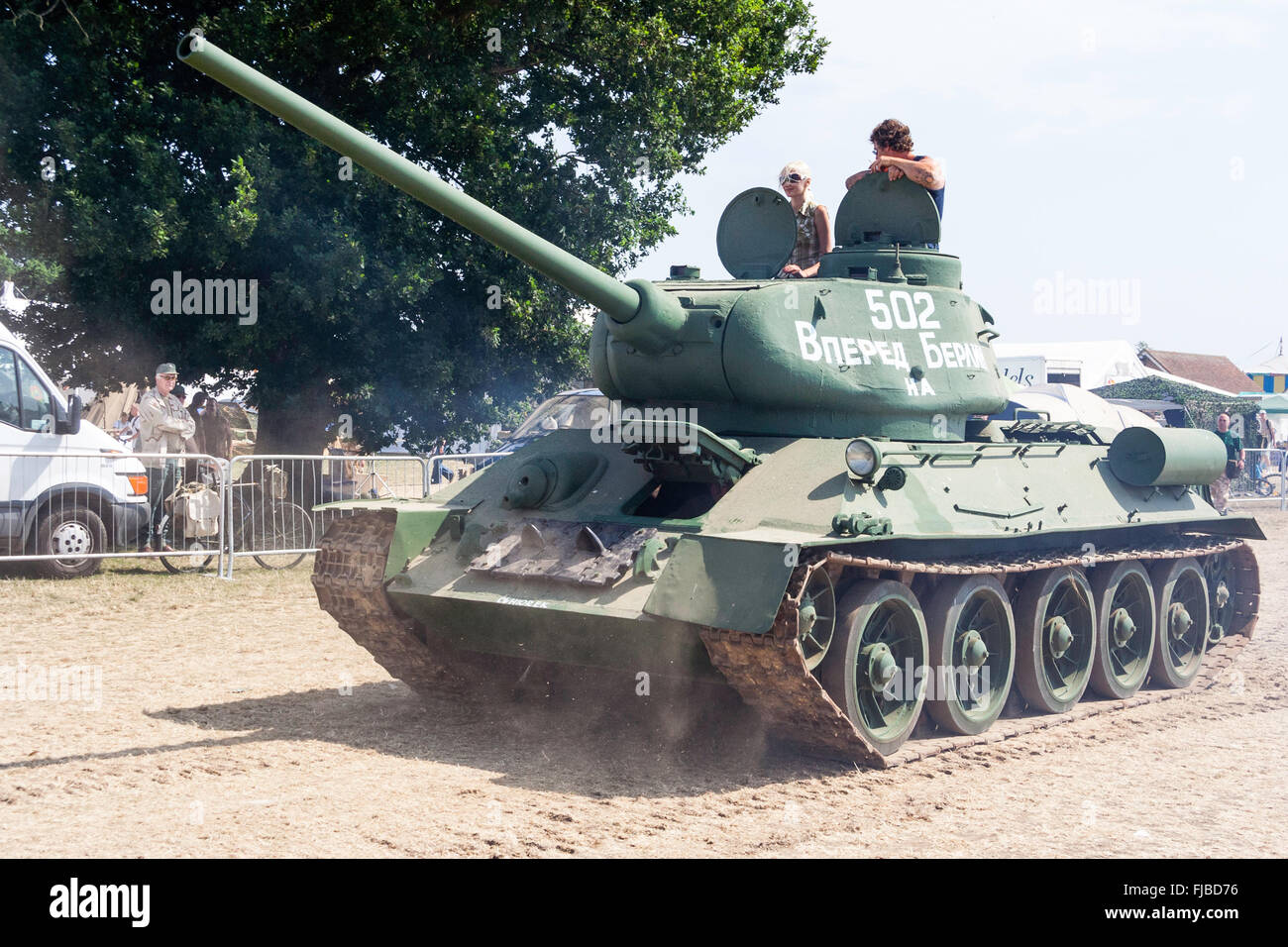 Krieg und Frieden zeigen, England. Zweiten Weltkrieg russische T-34 Panzer fahren entlang eingezäunt Feldweg und kicking up dust. Mann und Frau im Turm. Stockfoto