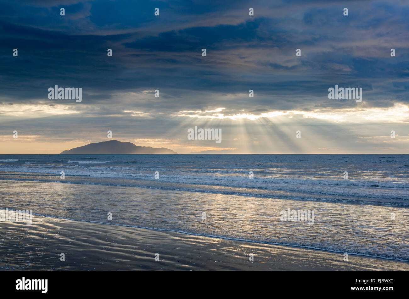 Abend Stimmung auf einem sandigen Strand, Wellen, Sonnenlicht durch dramatische Wolken strömen, Ost Küste, Nordinsel, Neuseeland Stockfoto
