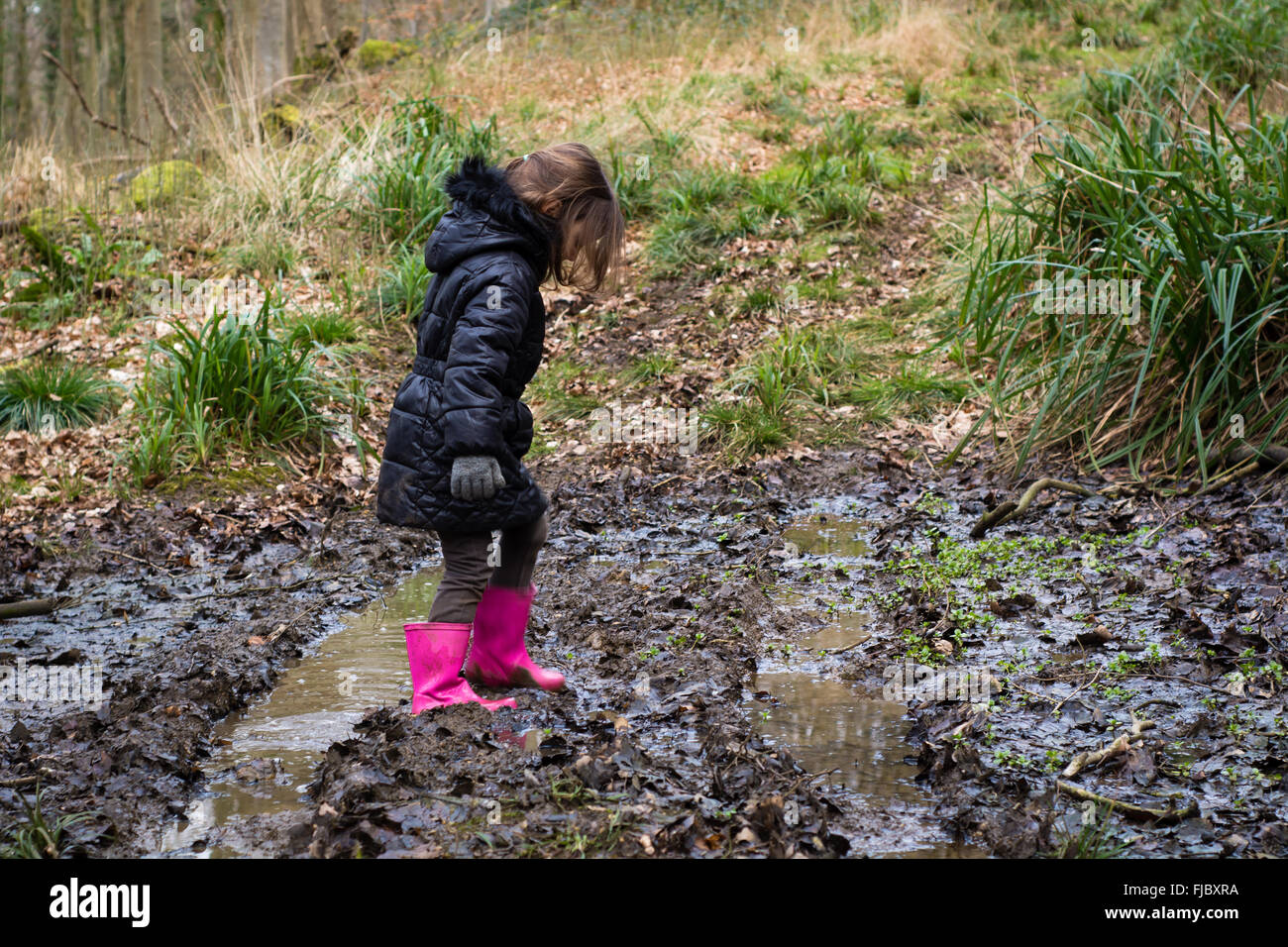 Kind im Schlamm auf dem richtigen Weg durch den Wald. Ein junges Mädchen in rosa Gummistiefel geht durch Schlamm in einem britischen Holz Stockfoto