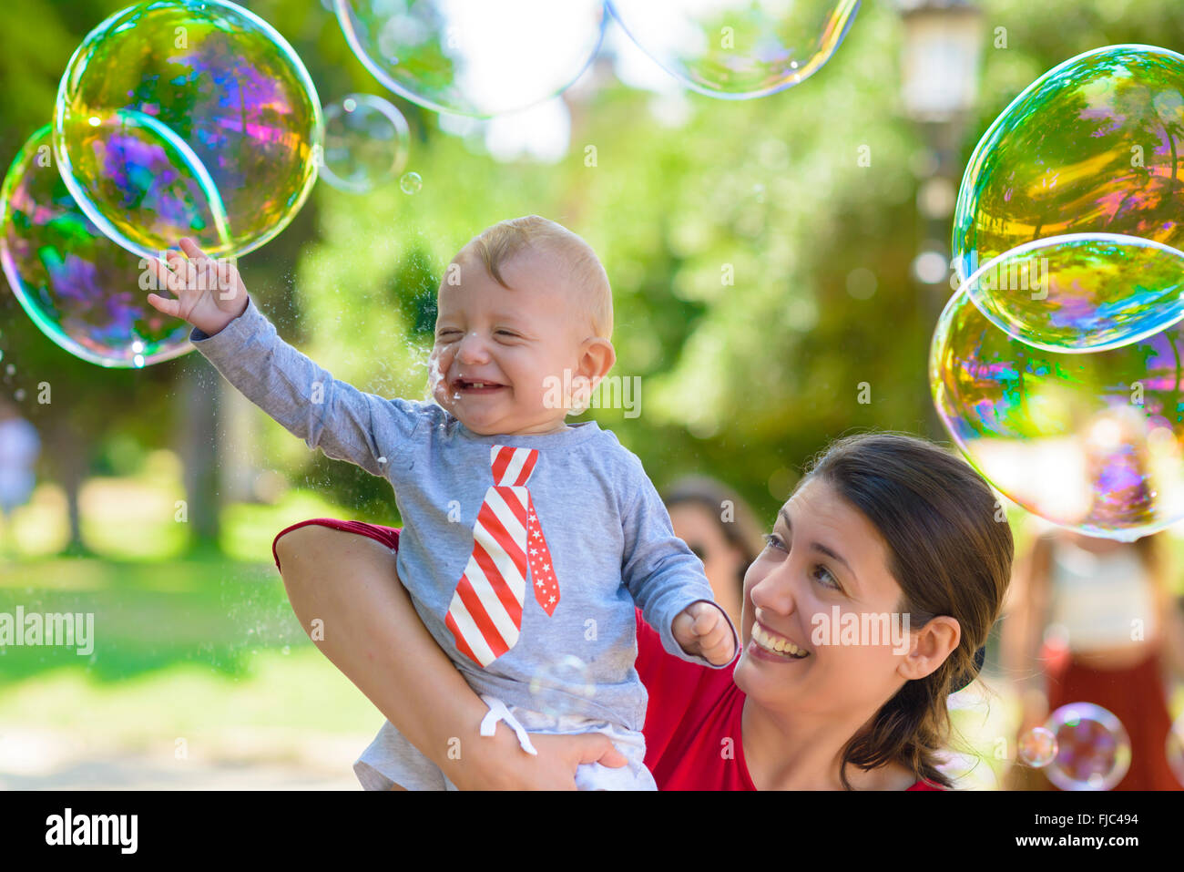 Niedliche Baby und seine Mutter fangen Seifenblasen an einem Sommertag Stockfoto