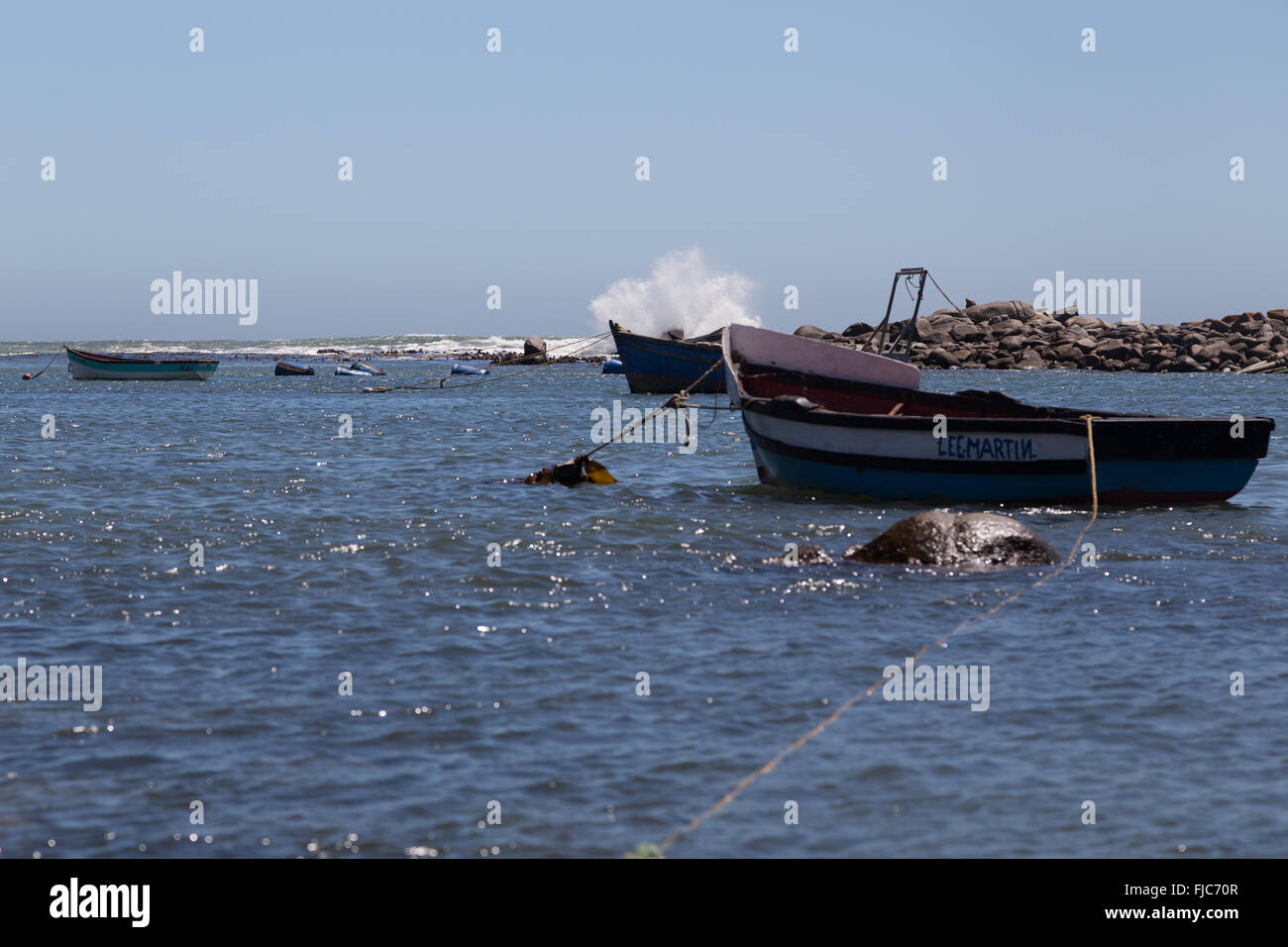 Ein kleines Fischerboot vor Anker sicher im geschützten Hafen von Jacobsbaai während Wellen an den Felsen brechen Stockfoto