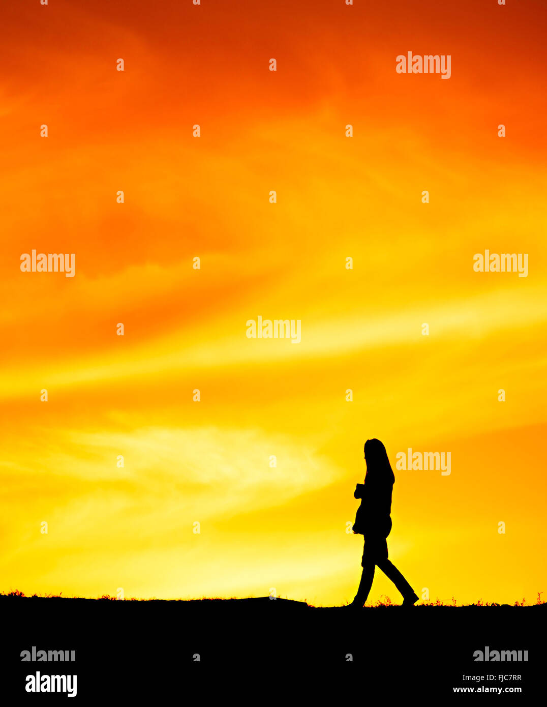 SIlhouette einer einsamen Frau zu Fuß bei Sonnenuntergang auf einem Hügel Stockfoto