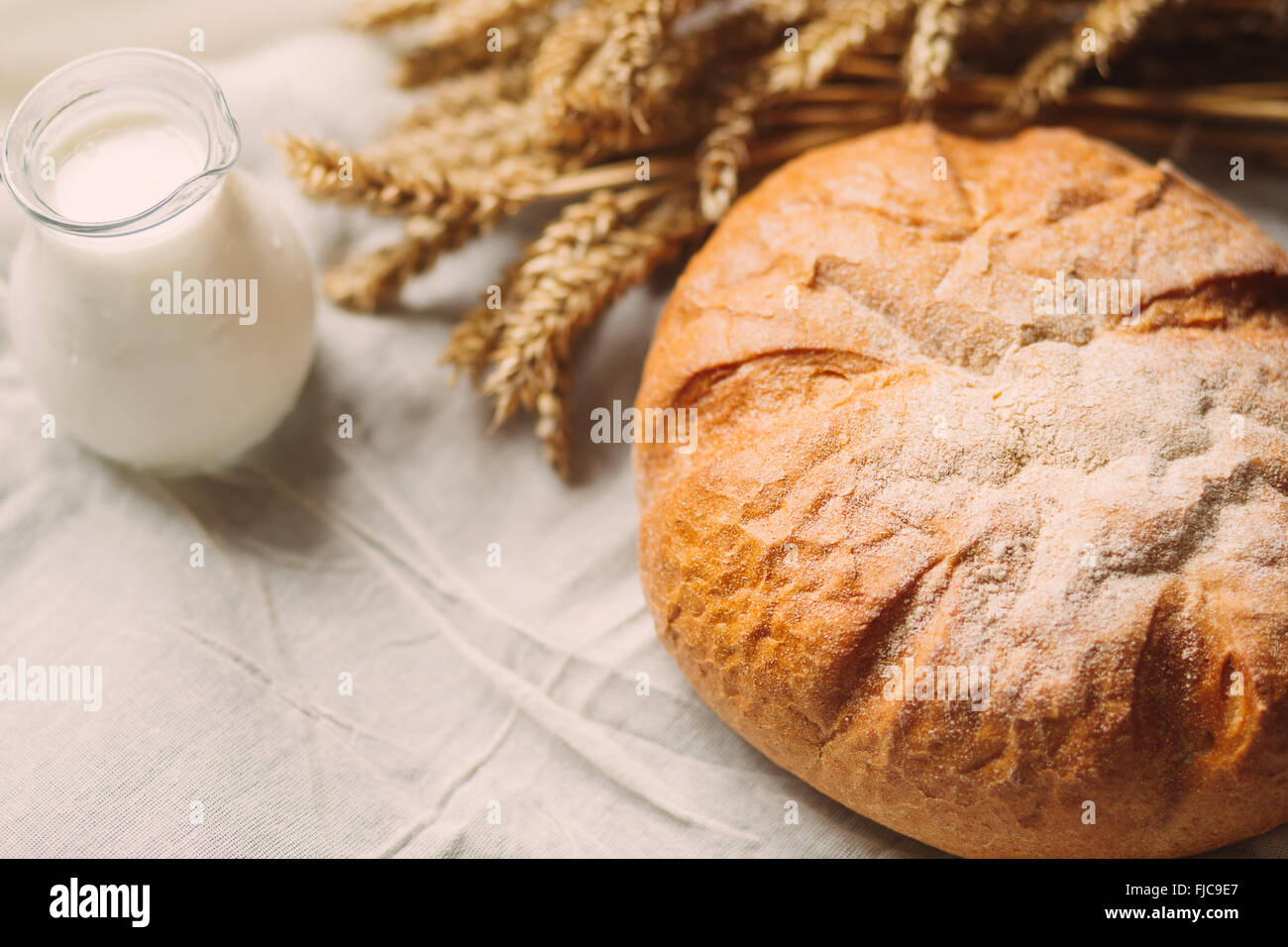 Glaskanne mit Milch und Brot auf weißen Textilien Stockfoto