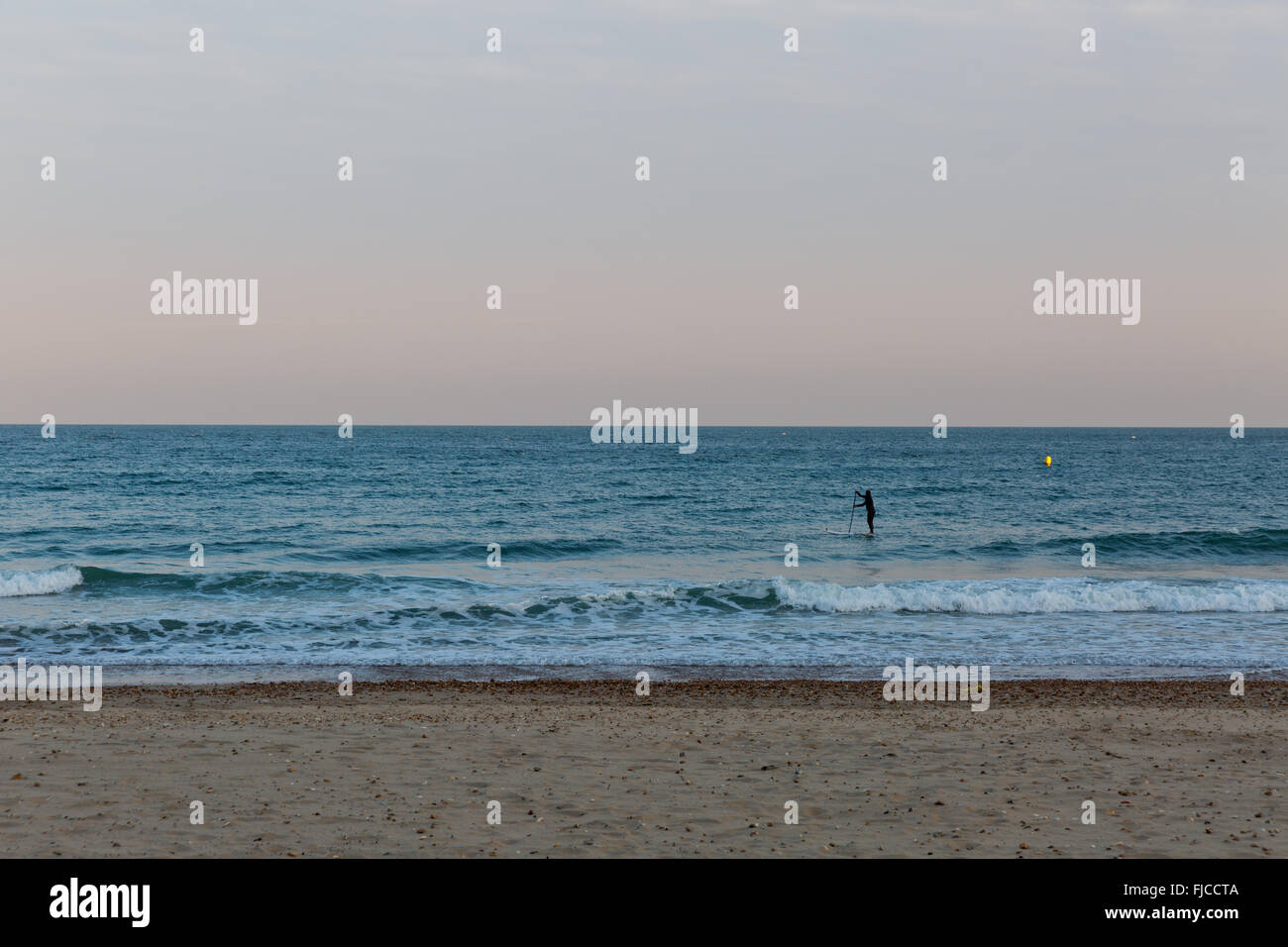 Goldene Abendlicht einer Silhouette eines Surfers auf seinem Brett, das Meer am Strand mit Sand und keine Wolken in Richtung der Stockfoto
