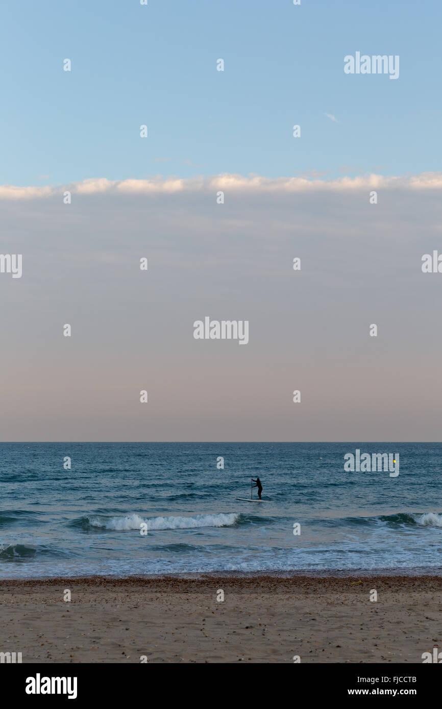 Goldene Abendlicht einer Silhouette eines Surfers auf seinem Brett, das Meer am Strand mit Sand und keine Wolken in Richtung der Stockfoto