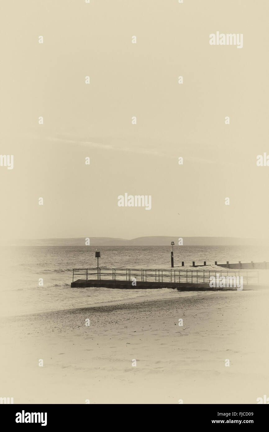 Ein schwarz-weiß Foto von einem Sonnenuntergang Licht, Blick auf einem Pier, aufgenommen am Strand mit Sand und eine Flugzeug-Wolke schräg in die Stockfoto