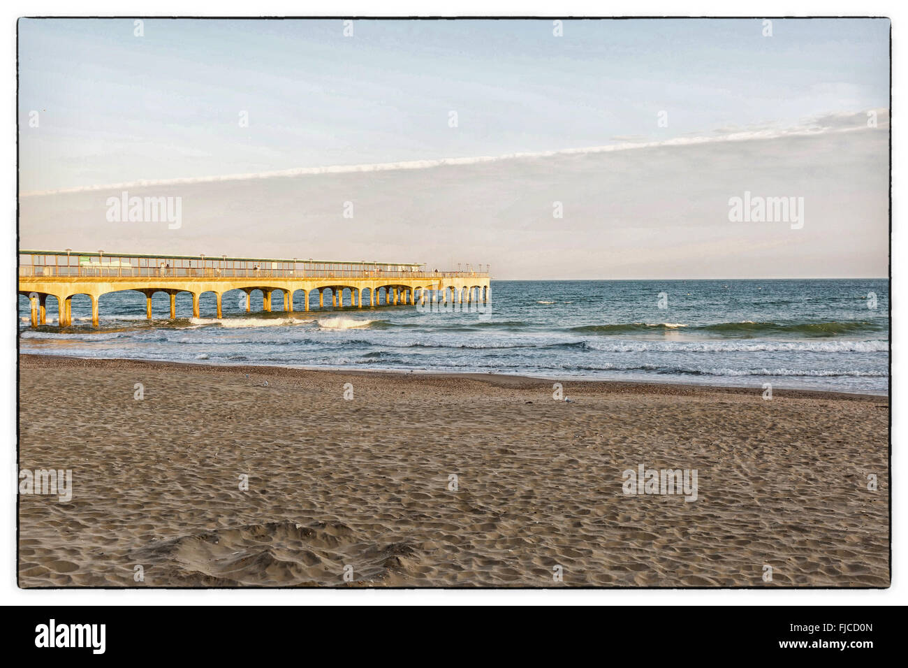 Ein farbiges Bild von einem goldenen Abendlicht mit rosa Tönung, Blick auf einem Pier am Strand mit Sand und ein Flugzeug-Cloud auf ein angl Stockfoto