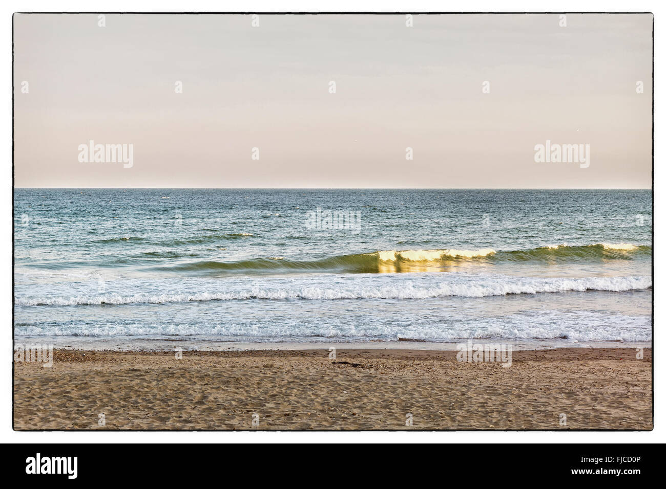 Ein farbiges Bild der goldenen Abendlicht mit rosa Tönung, Blick auf die Wellen am Strand mit Sand und einem keine Wolken in der sk Stockfoto