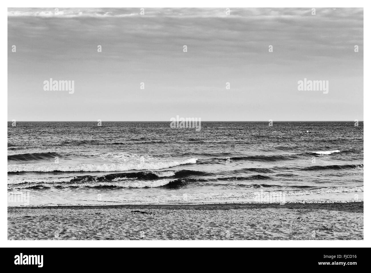 Ein schwarz-weiß Bild von einem Sonnenuntergang Sommerlicht, Blick auf die Wellen am Strand mit Sand und einem keine Wolken am Himmel in Eur Stockfoto