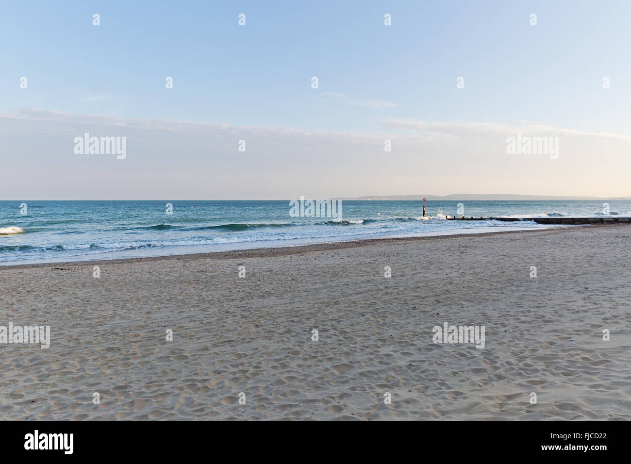 Goldene Abendlicht einer Silhouette eines Surfers auf seinem Brett, das Meer am Strand mit Sand und keine Wolken in Richtung der Stockfoto