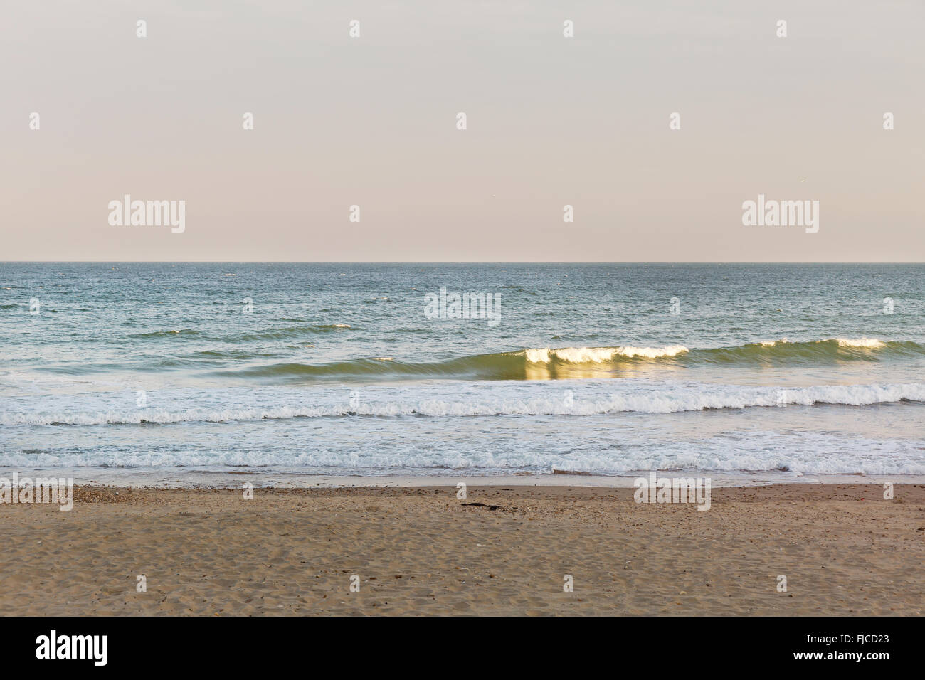 Goldene Abendlicht einer Silhouette eines Surfers auf seinem Brett, das Meer am Strand mit Sand und keine Wolken in Richtung der Stockfoto