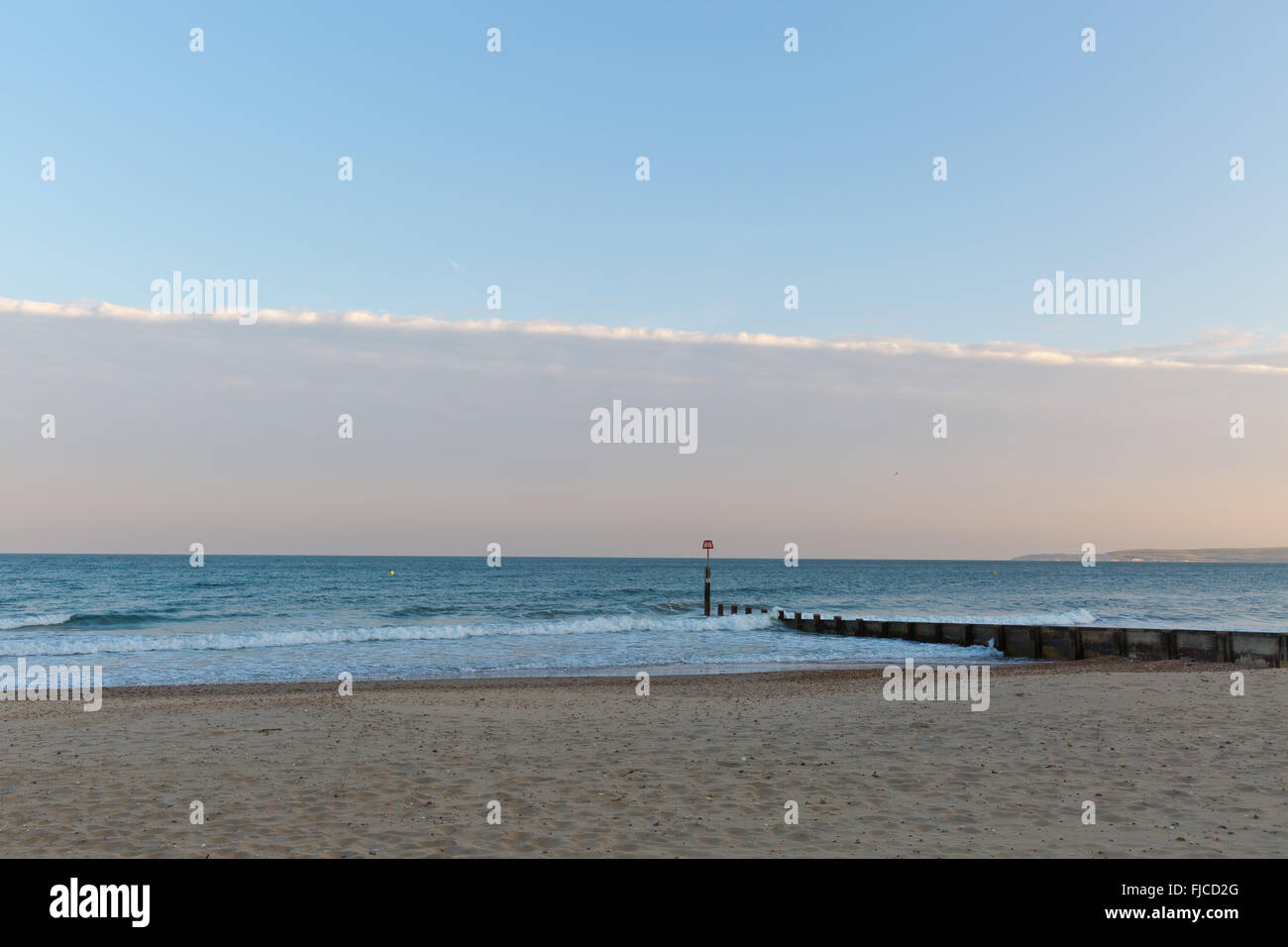 Goldene Abendlicht eines Piers mit Blick auf das Meer am Strand mit Sand und einem Streifen von Wolken am Himmel in Europa mit Stockfoto