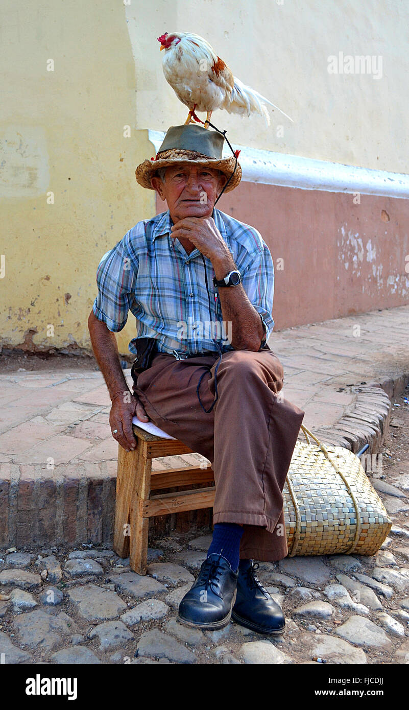 Mann, sitzend mit einem Huhn auf dem Kopf in Trinidad, Kuba Stockfoto
