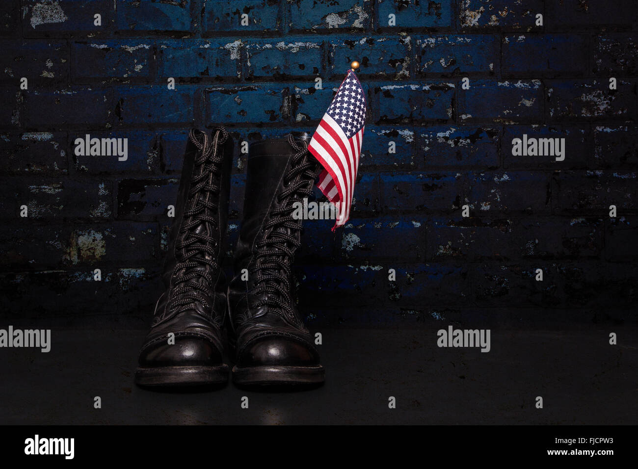 Ein paar Springerstiefel mit einer kleinen amerikanischen Flagge auf einem blauen Backstein-Hintergrund. Stockfoto