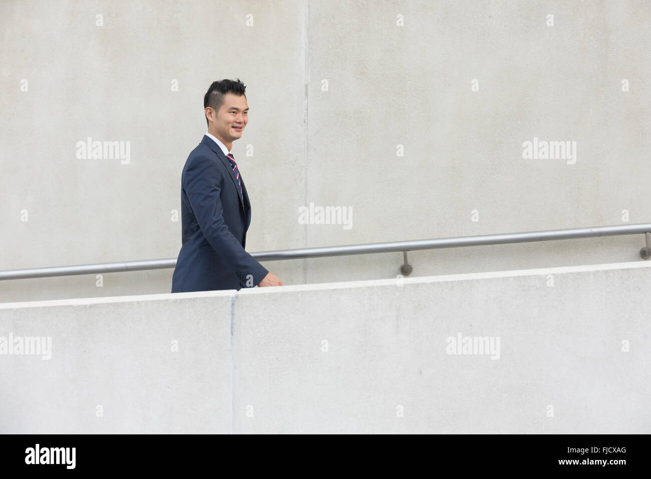 Seitenansicht eines glücklich asiatischen Geschäftsmann zu Fuß auf der Stadtstraße. Stockfoto
