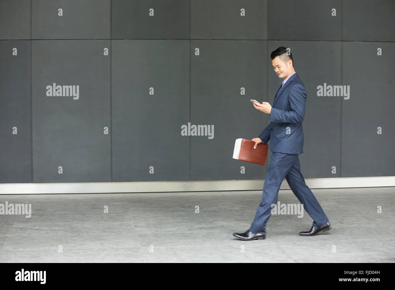 Seitenansicht eines chinesischen Geschäftsmannes walking im Freien und mit seinem Smartphone in modernen asiatischen Stadt. Geschäft auf dem Go Konzept. Stockfoto