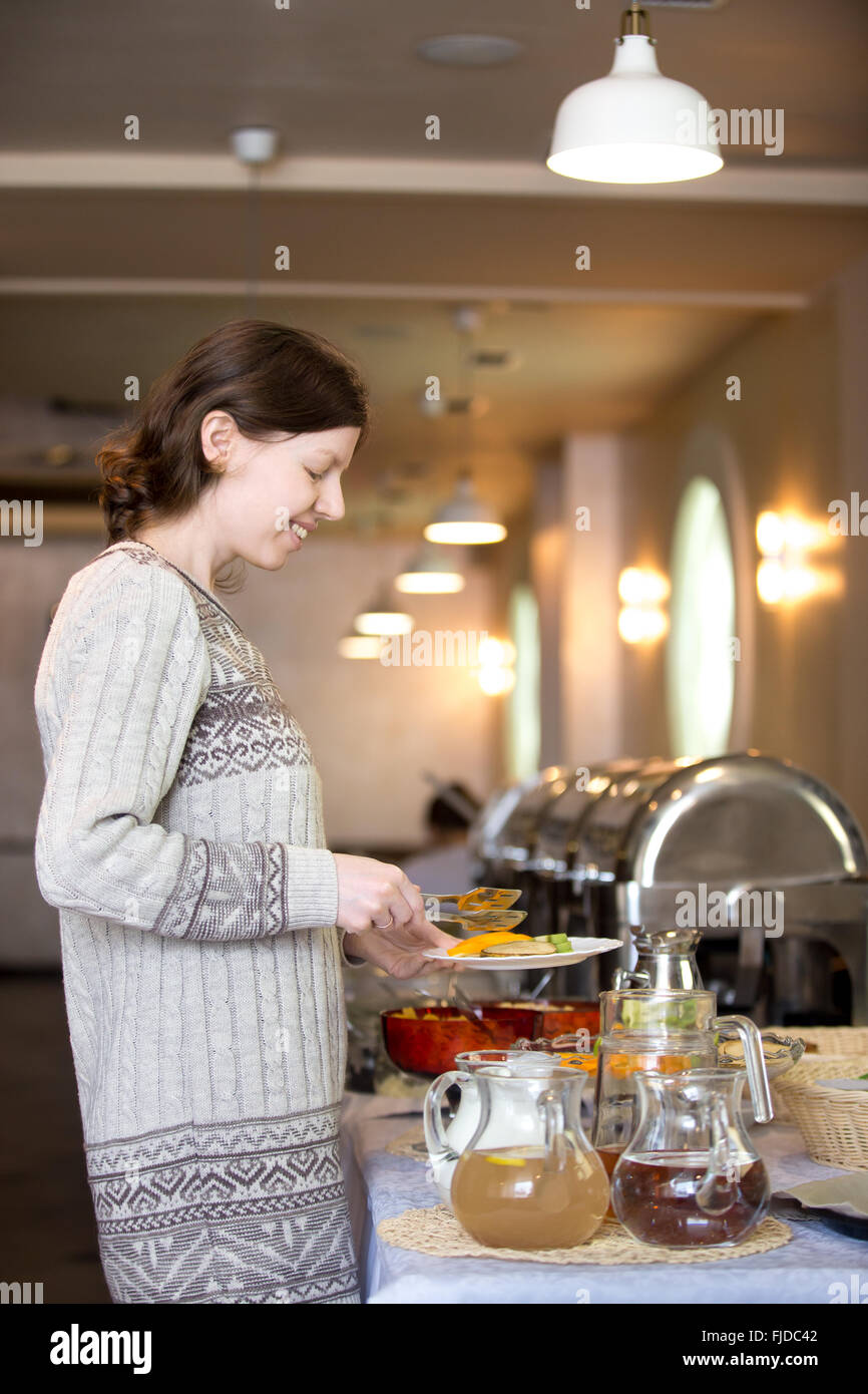 Porträt des jungen lässig fröhlich lächelnde Frau mit sich selbst Frühstücksbuffet im Hotelrestaurant am Morgen Stockfoto