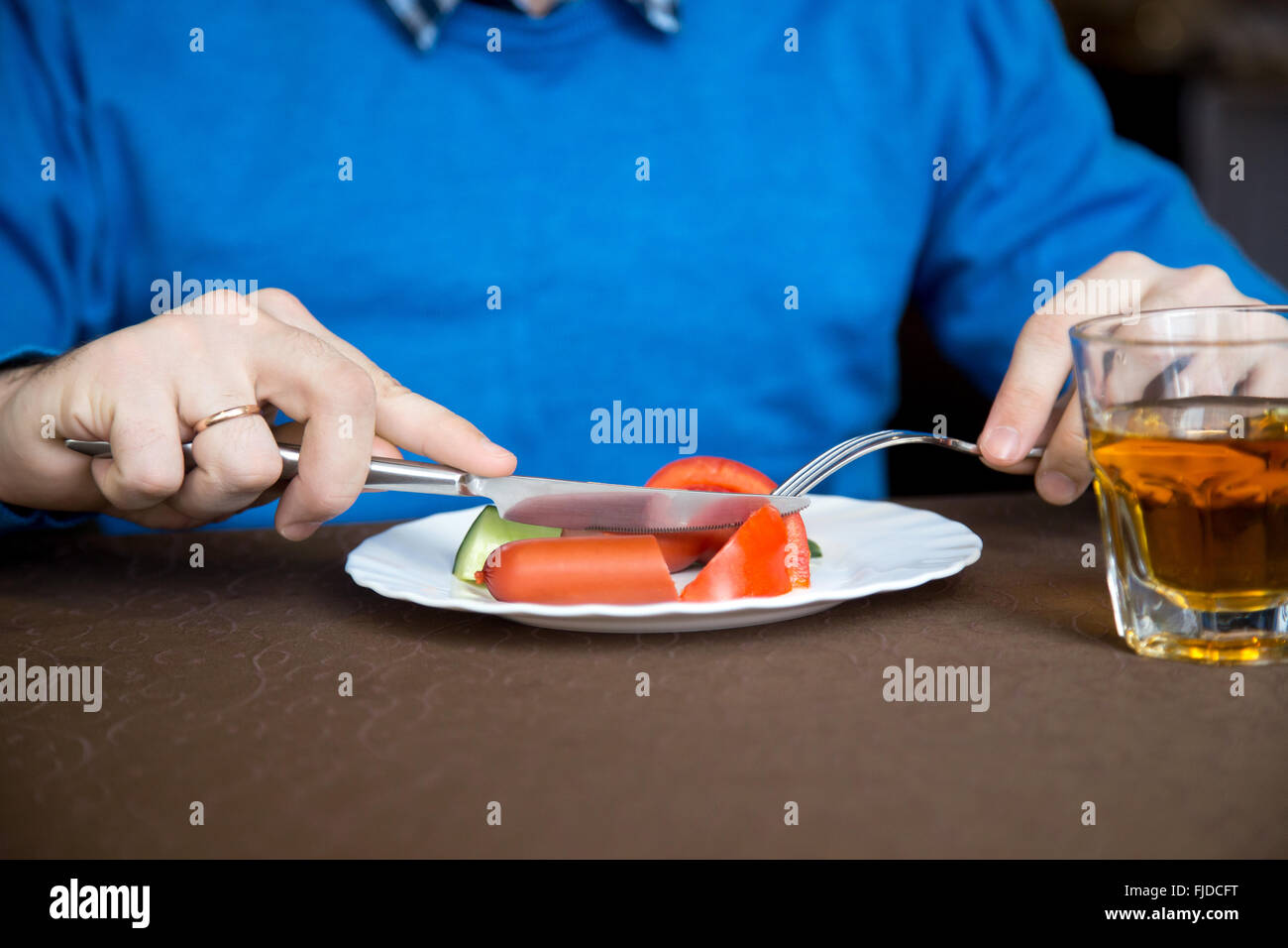 Junger Mann drinnen essen Gemüse mit Wurst mit Messer und Gabel, close-up der Hände Stockfoto