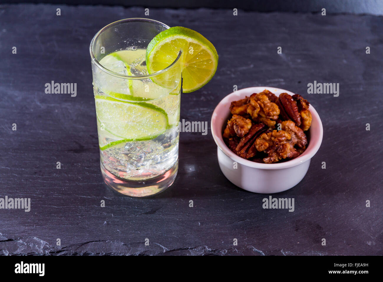Gin und Tonic mit Kalk, garniert mit Schale nach Hause gerösteten Nüssen serviert. Stockfoto