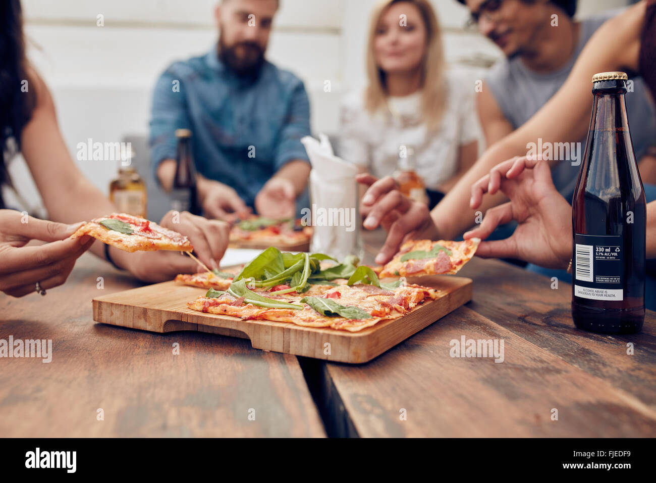 Schuss von Pizza am Tisch, mit einer Gruppe junger Leute herumsitzen und hob einen Teil hautnah. Freunden feiern und Essen Stockfoto