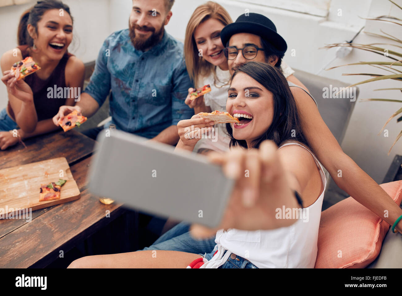 Gruppe von Rassen junge Menschen dabei, dass eine Selfie Pizza essen. Junge Frau, die ihre Freunde sitzen während Pizza essen Stockfoto