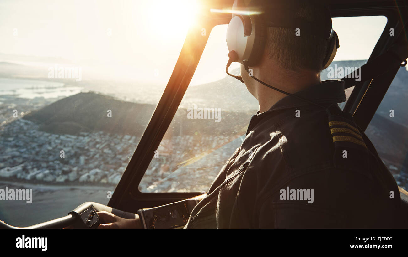 Nahaufnahme eines männlichen Piloten fliegen eines Hubschraubers und suchen vor dem Fenster mit Sonne Flare Eintritt in das Cockpit. Stockfoto