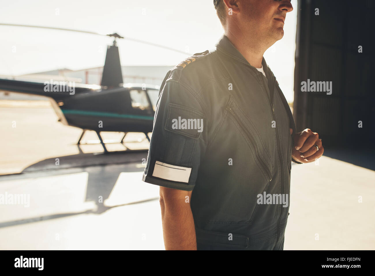 Porträt von professionellen Piloten im einheitlichen stehen im Flugzeughangar mit einem Hubschrauber im Hintergrund abgeschnitten Stockfoto