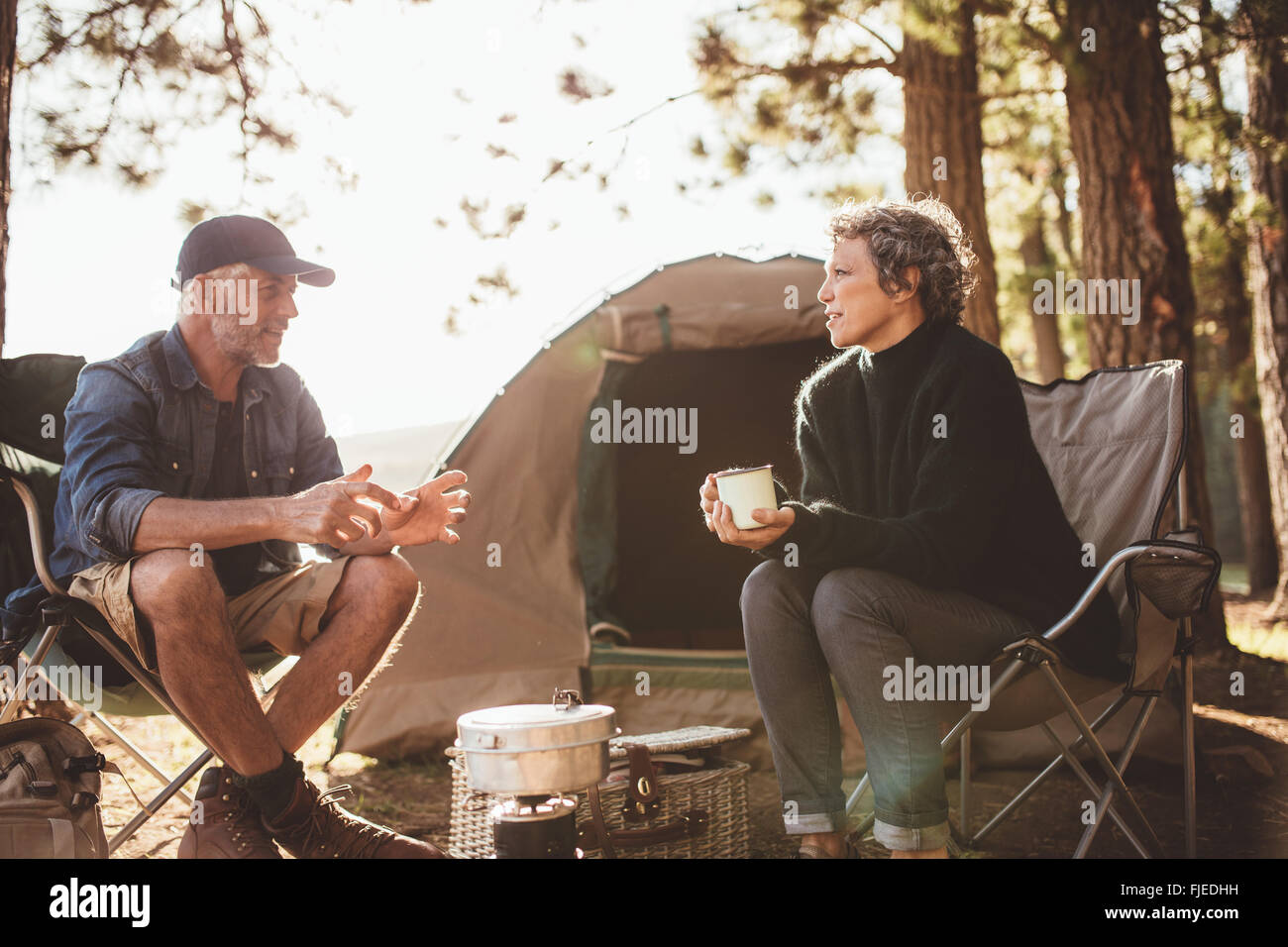 Reifer Mann und Frau sitzen und reden auf einem Campingplatz. Älteres paar sitzen auf Stühlen außerhalb des Zeltes an einem Sommertag. Stockfoto