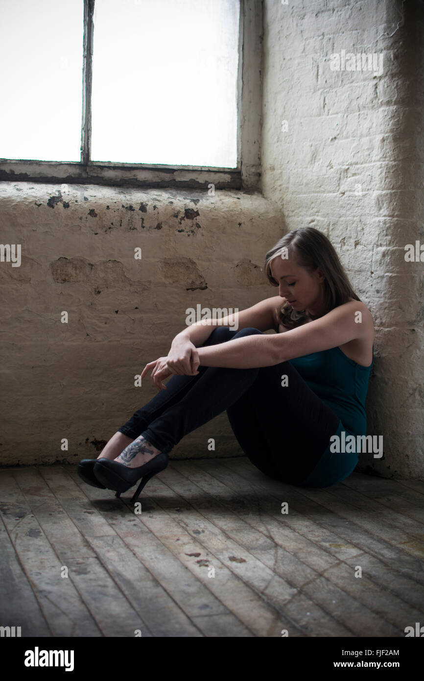 Traurige junge Frau saß auf dem Holzboden am Fenster Stockfoto