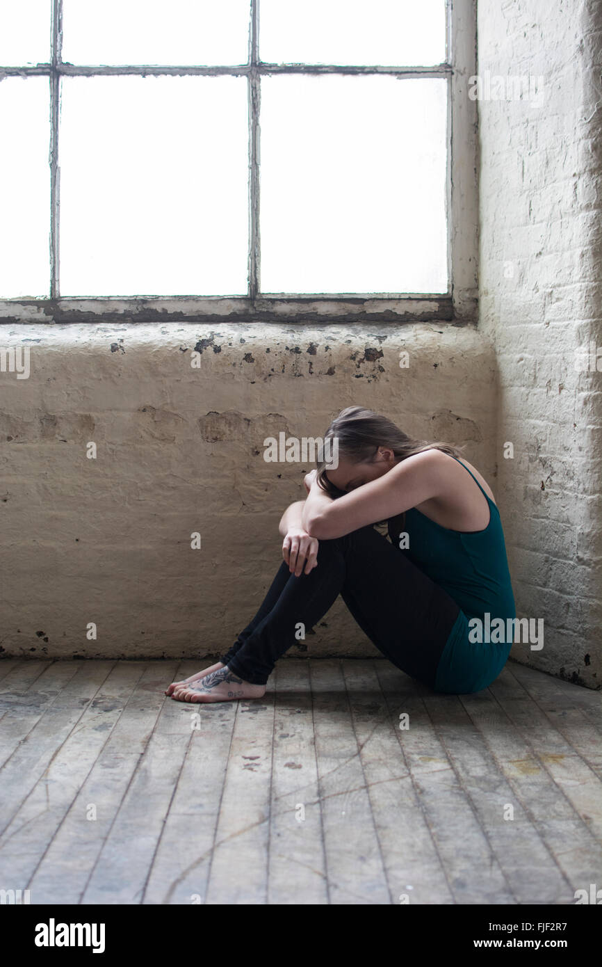 Traurige junge Frau saß auf dem Holzboden am Fenster Stockfoto