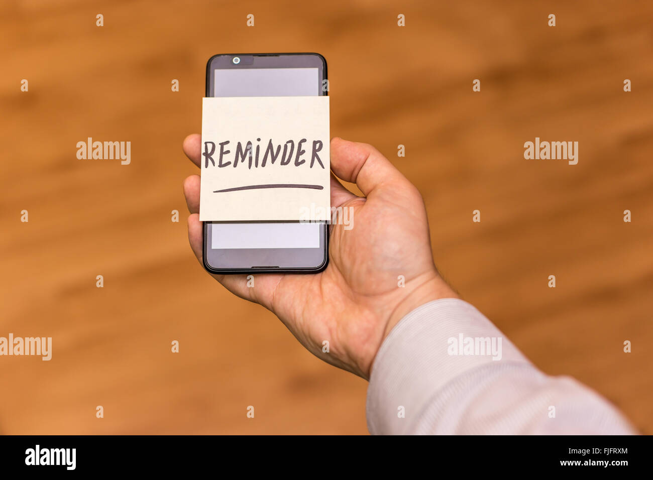 Menschliche Hand mit einem Smartphone mit gelben Hinweis darauf geklebt. Der Word Reminder ist auf dem Zettel geschrieben. Stockfoto