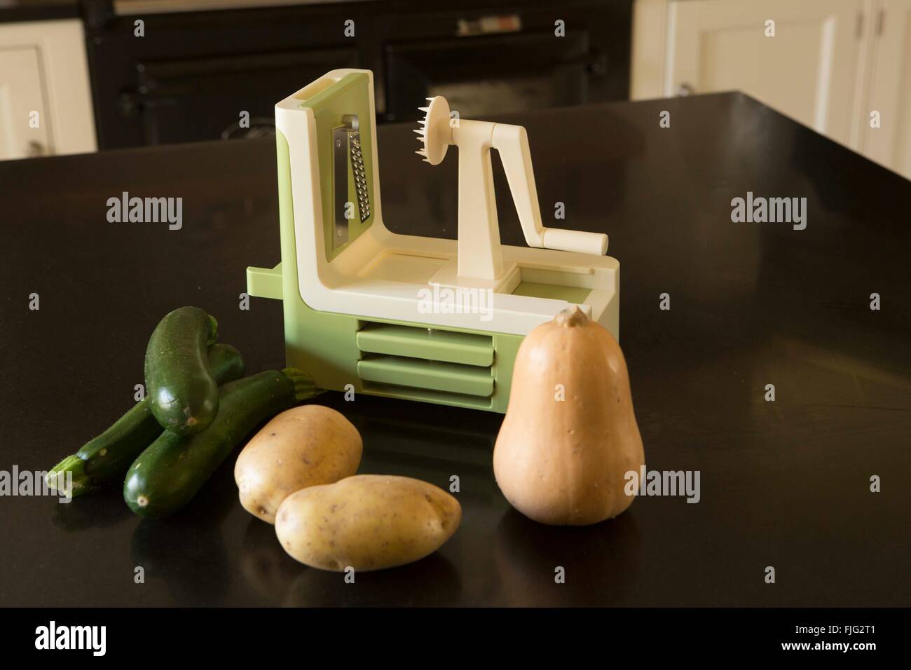 Eine glänzende neue Spiralizer sitzt auf einem heimischen Küche Arbeitsplatte neben Butternut-Kürbis, Zucchini und Kartoffeln. Stockfoto