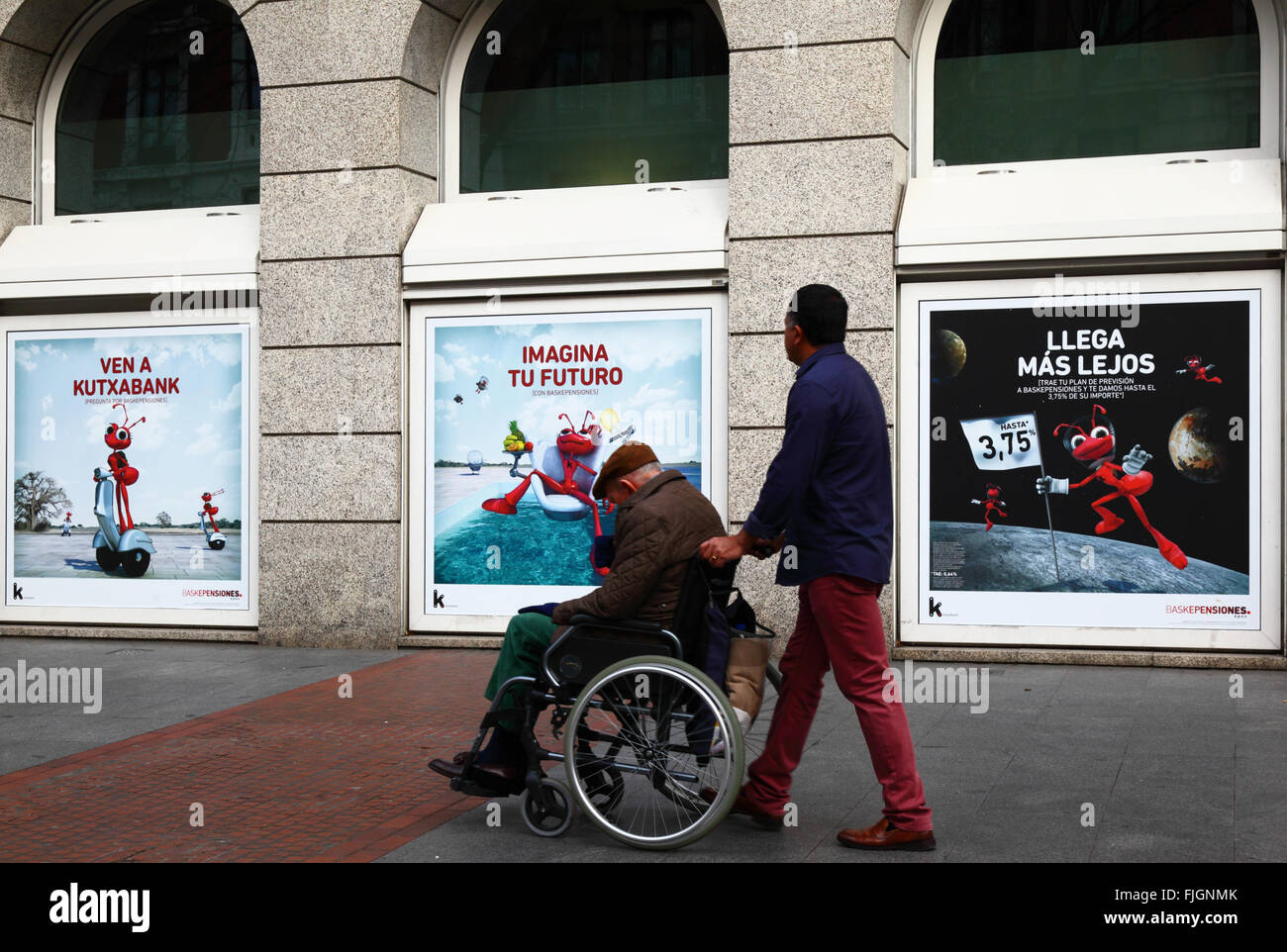 Mann schob Rentner im Rollstuhl, die letzten anzeigen für Baskepensiones Pensionspläne auf Kutxabank Gebäude, Bilbao, Spanien Stockfoto