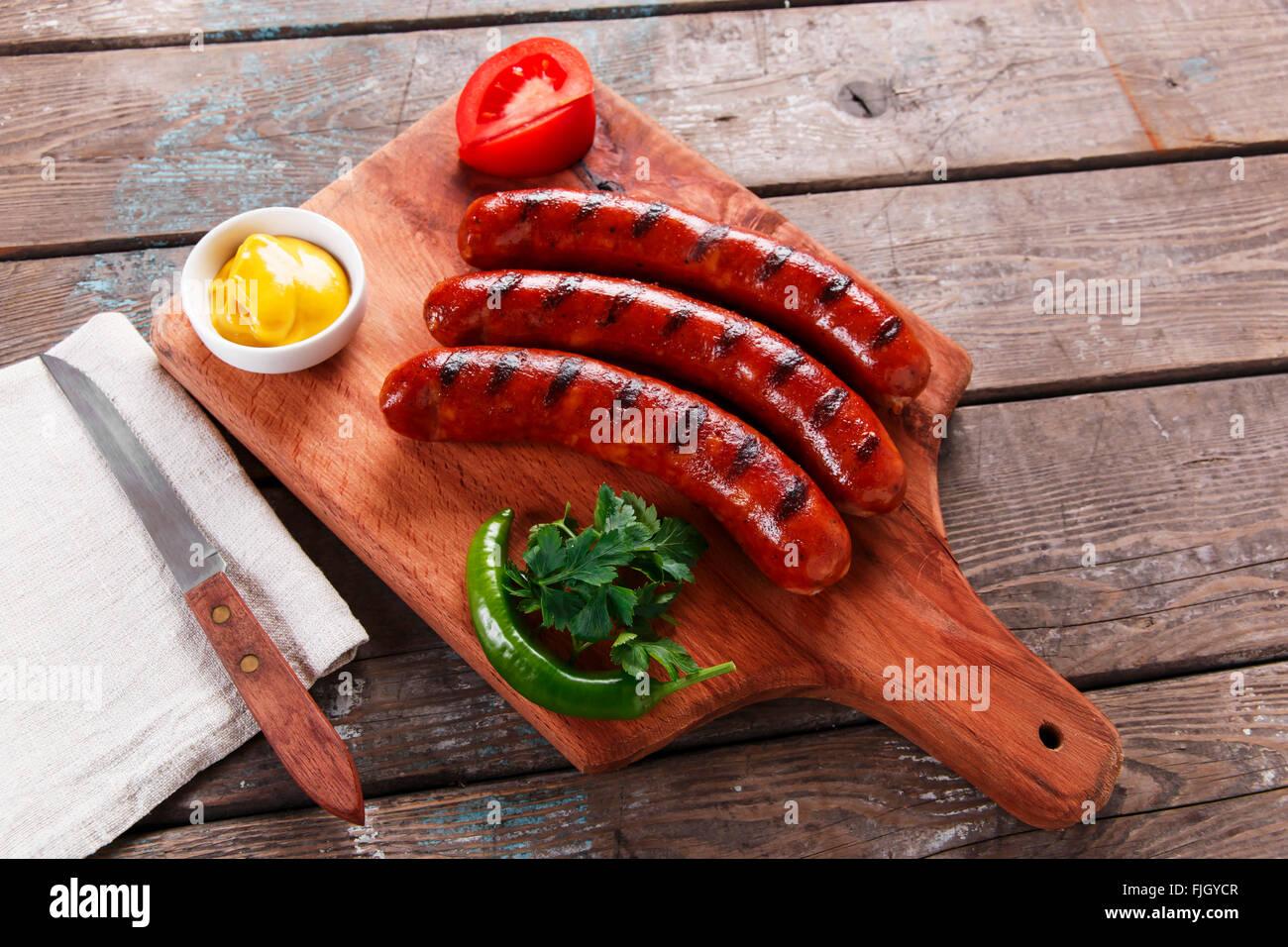 Gegrillte Wurst auf einem Holzbrett mit Sauce und Gemüse Stockfoto