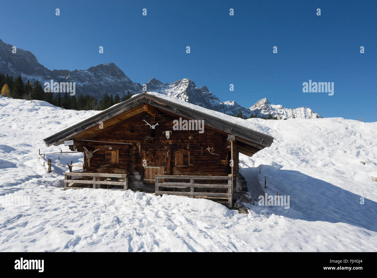 Schneebedeckte alpine Holzchalet auf der Ladiz-Alm mit den Klippen das Karwendelgebirge bei strahlendem Sonnenschein, Tirol, Österreich Stockfoto