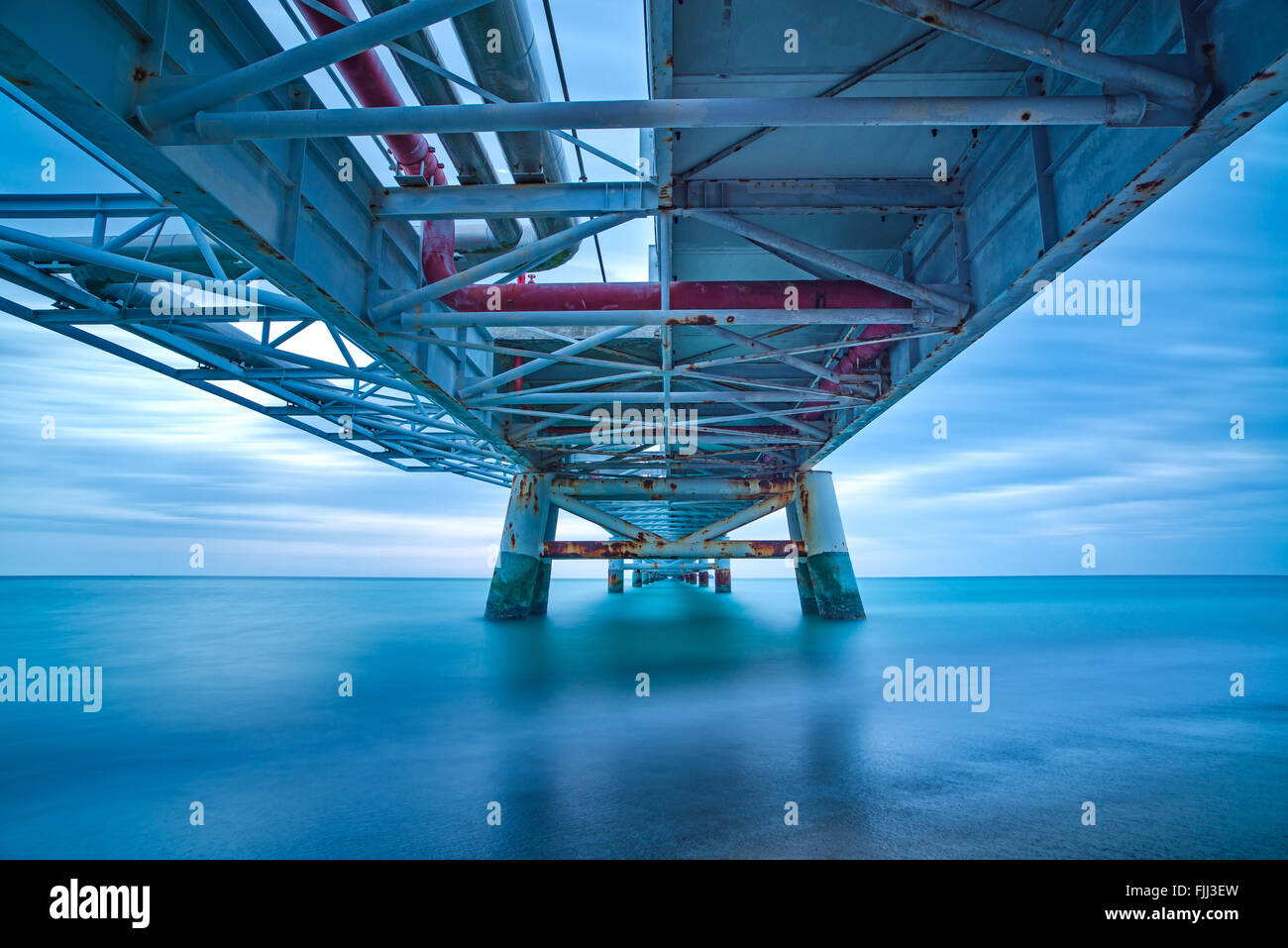 Industrielle Pier auf den Meereshorizont. Ansicht von unten. Langzeitbelichtung Fotografie an einem bewölkten Tag. Stockfoto