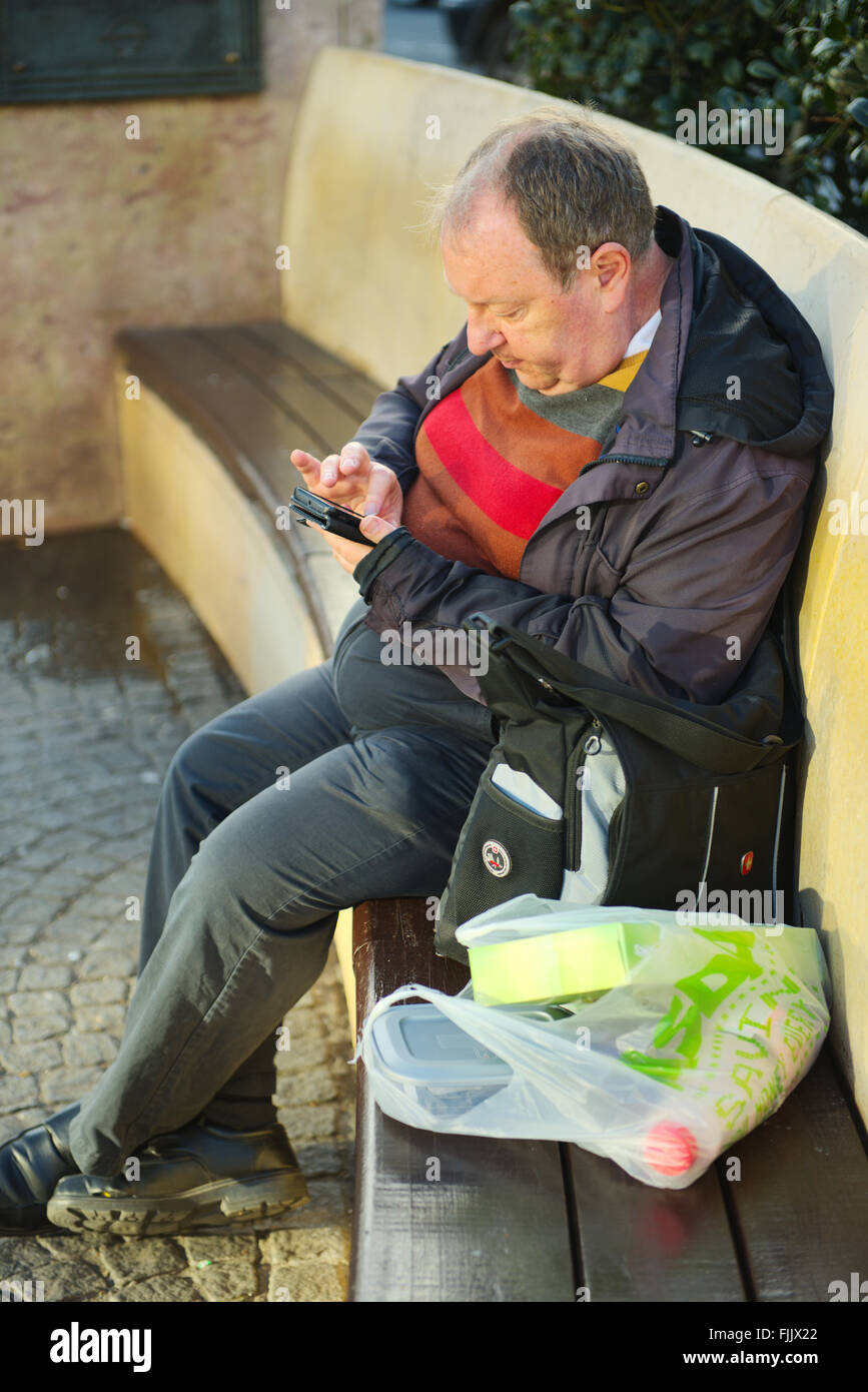 Mittleren Alter Mann sitzt auf Sitzbank mit Einkaufs- und Handy Stockfoto