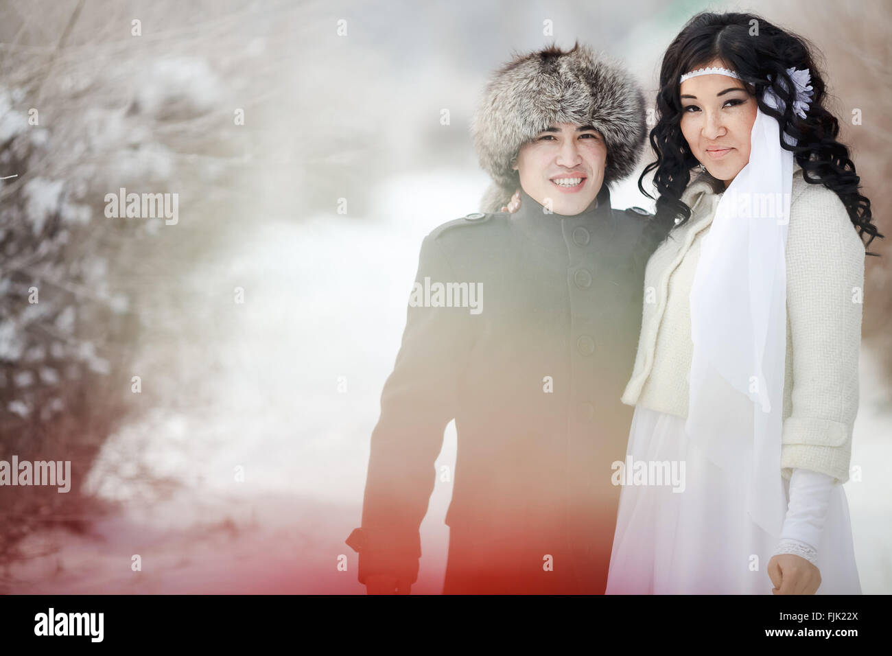 Winterhochzeit, exotische asiatische Paar Brautpaar, Bräutigam in Pelzmütze, Braut trägt Wintermantel. Stockfoto