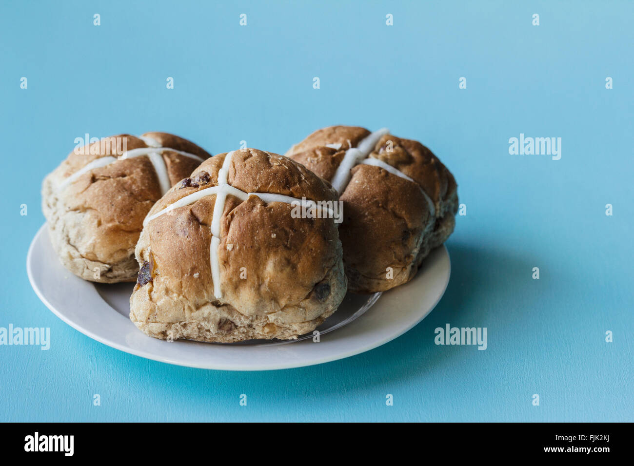 Drei Ostern Hot Cross Buns auf einem weißen Teller auf blauem Hintergrund Stockfoto