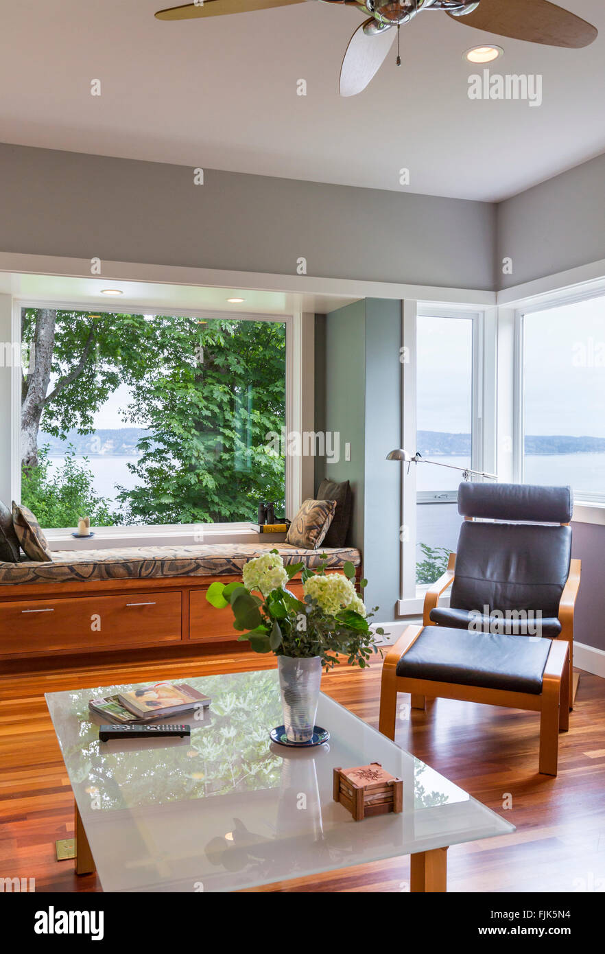 Zeitgenössische gehobene heimische Wohnzimmer mit Leder-Lounge-Sessel, Couchtisch aus Glas, Fensterbank und Fenster mit Blick auf das Wasser Stockfoto