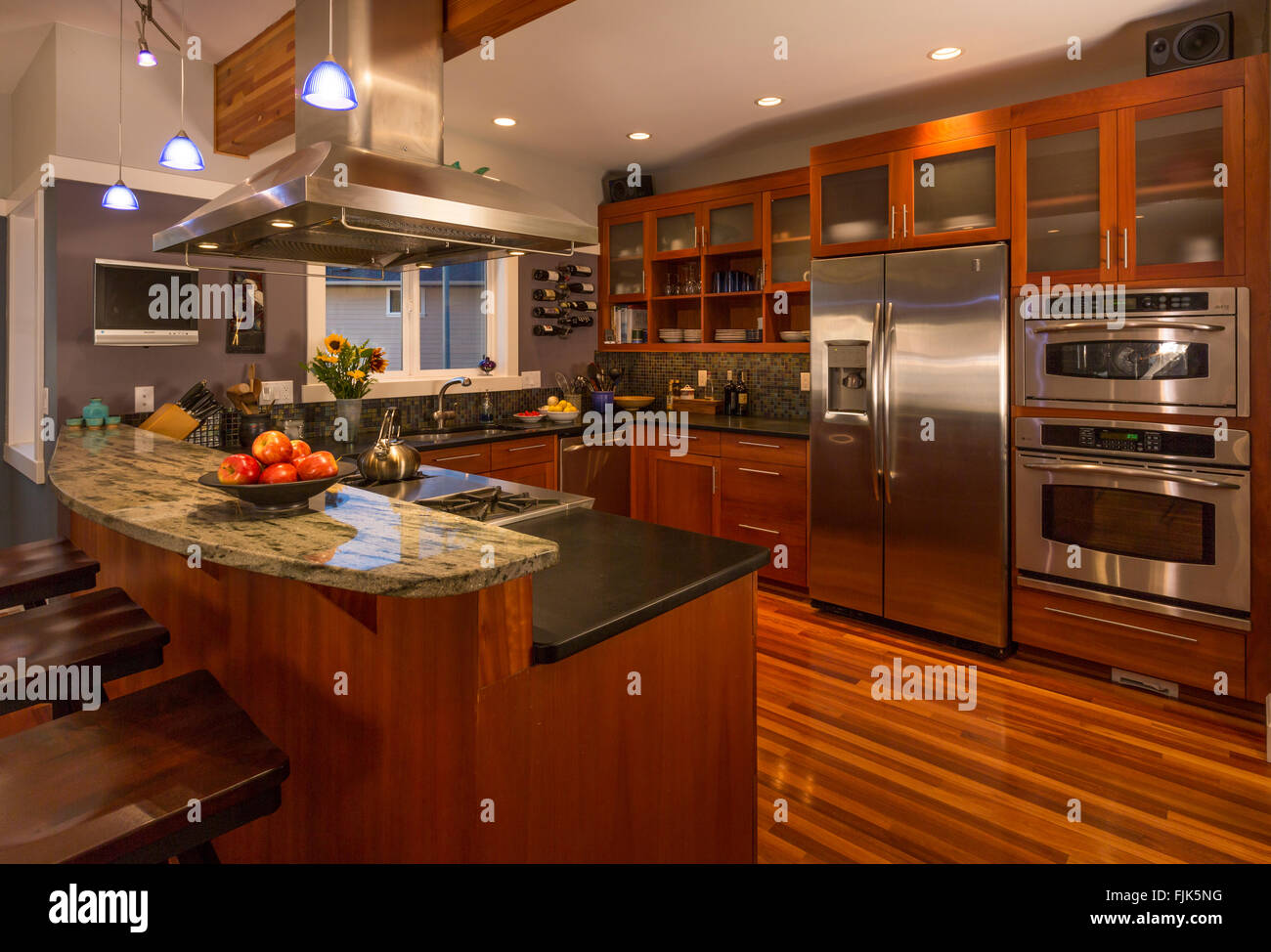 Zeitgenössische gehobene Küche zu Hause Innenraum mit Holz Schränke & Fußböden, Arbeitsplatten aus Granit, Edelstahl Geräte- und Akzentbeleuchtung Stockfoto