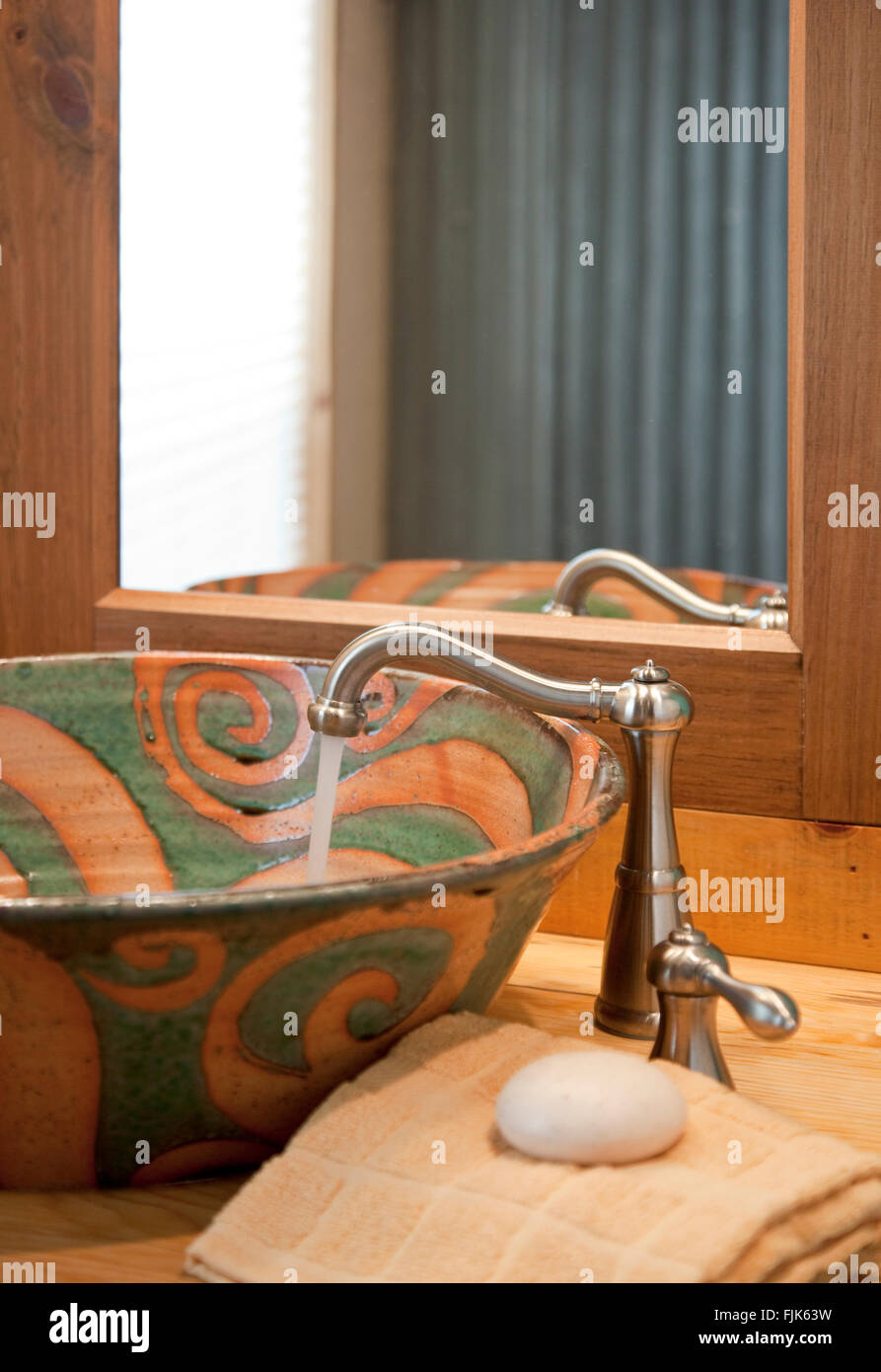 Läuft Wasser aus einem Edelstahl Wasserhahn in eine handgefertigte Keramik Waschbecken, Handtuch und Spiegel in einem kreativen home Bad Toilette Waschtisch Stockfoto