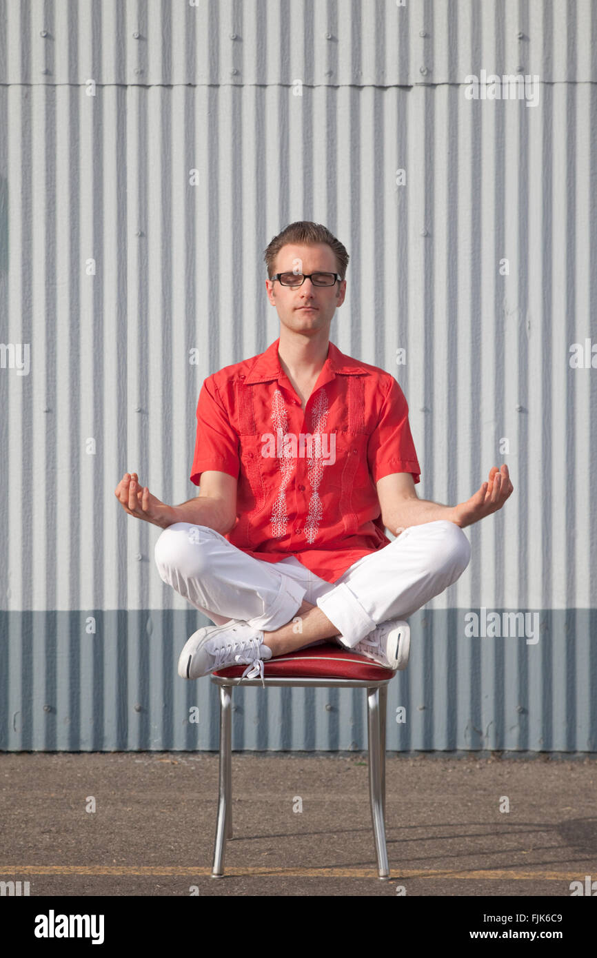 Hipster Mann in Retro Kleidung sitzen und meditieren, Yoga Position auf einen Stuhl. Amerikanische Geek Chic. Stockfoto