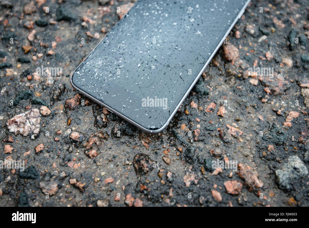 Telefon mit gebrochenen Bildschirm auf Asphalt. Gerät einer Person gelöscht. Glas bedeckt mit Schneeflocken. Stockfoto