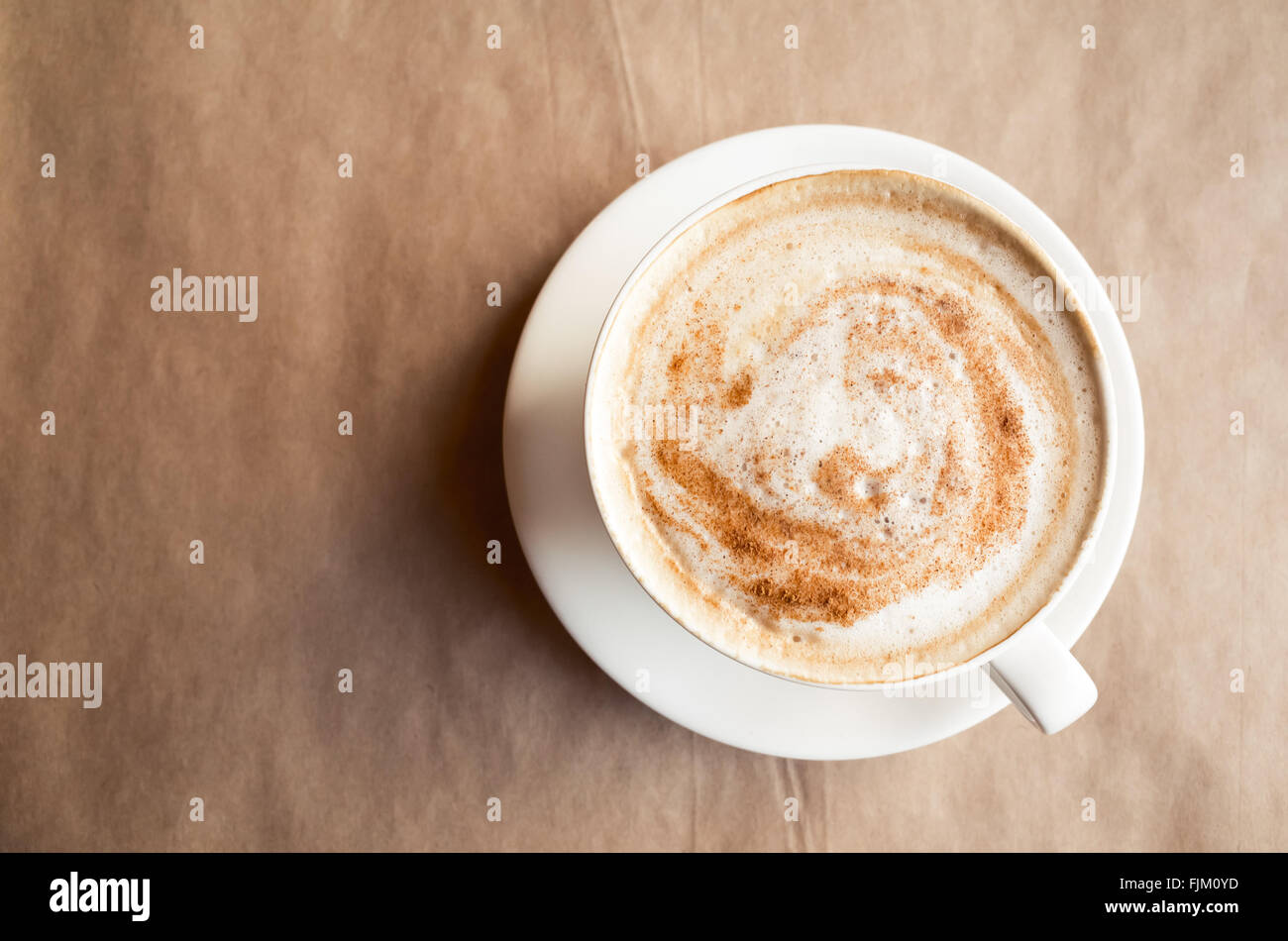 Cappuccino. Tasse Kaffee mit Milchschaum steht über Altpapier auf Tisch in der Cafeteria. Ansicht von oben Stockfoto